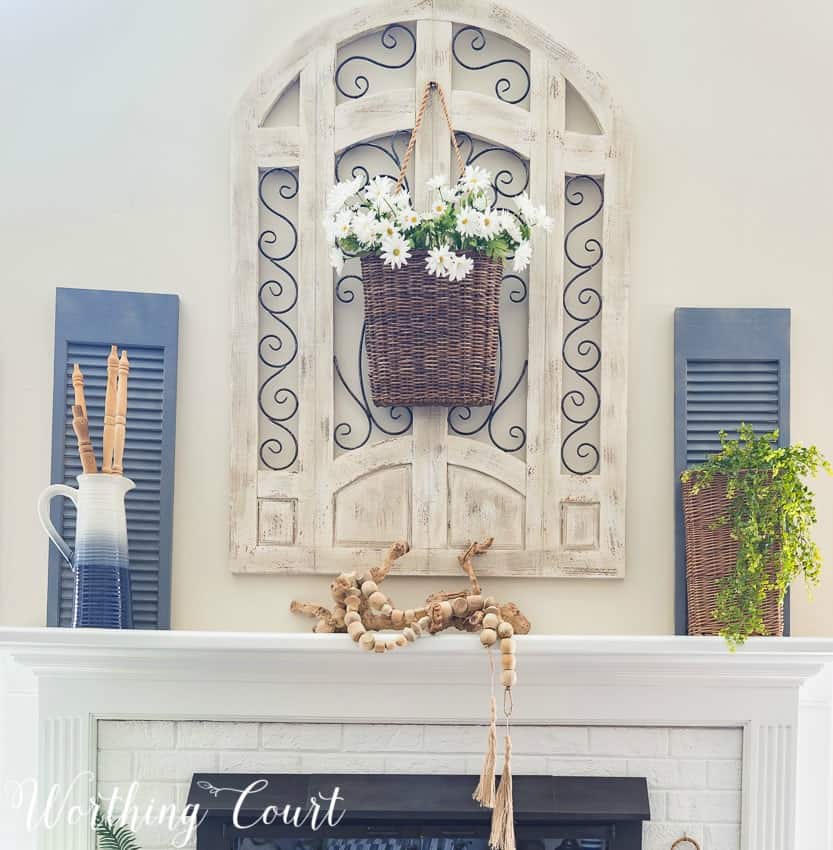 The mantel with a piece of driftwood on top flanked by a basket and a pitcher.