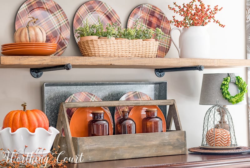 Fall shelf decorating ideas with plaid plates, brown glass bottles, pumpkins and a toolbox.