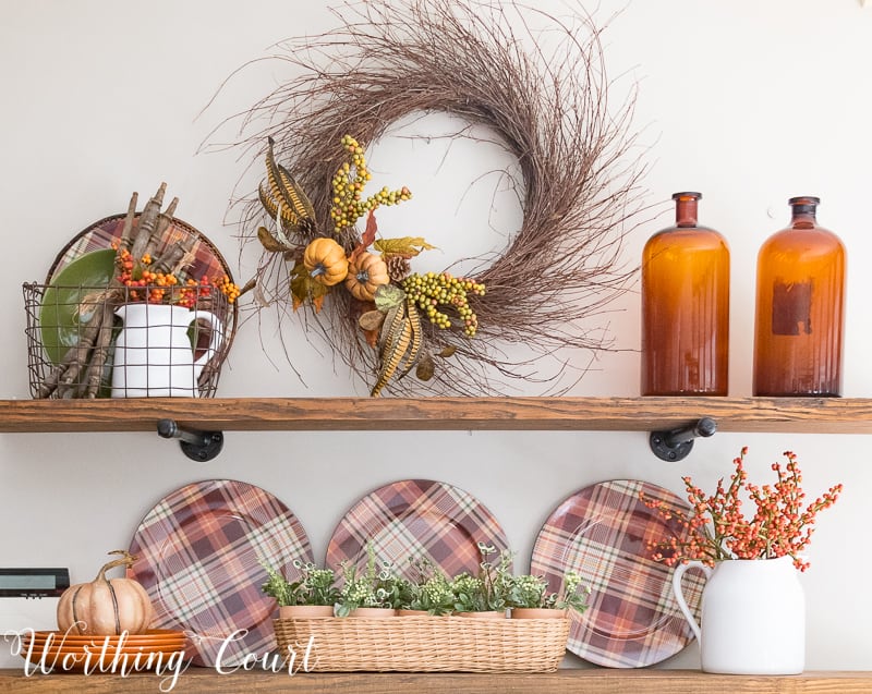 Rustic farmhouse open shelves decorated for fall with plaid plates, brown glass bottles and a grapevine wreath. 