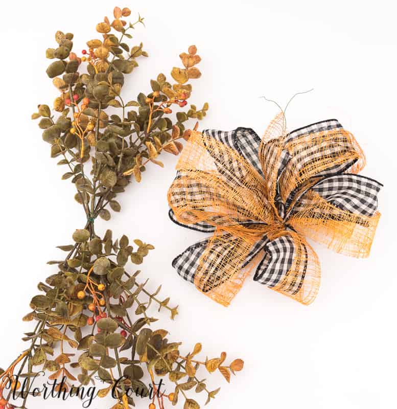 The ribbon tied into a bow and sprigs of berries on a branch laid out.