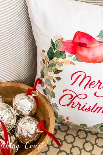 Merry Christmas pillow beside wood bowl filled with silver bells