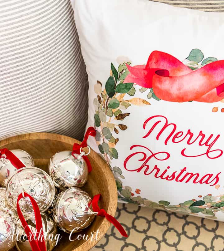 Merry Christmas pillow beside wood bowl filled with silver bells