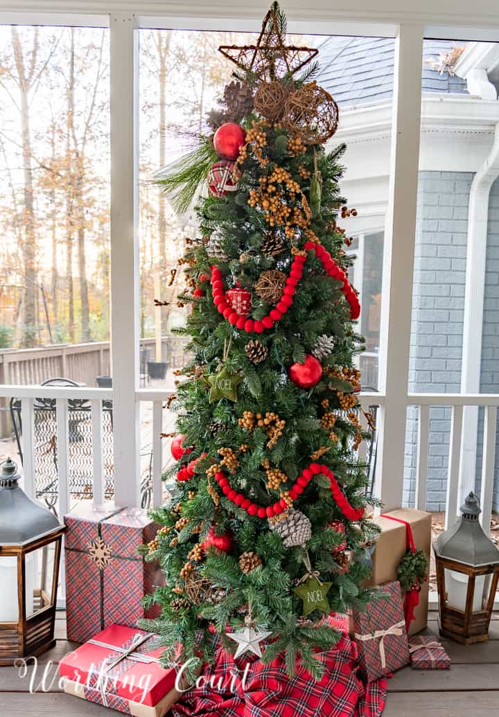 skinny Christmas tree on a screen porch decorated with outdoor type ornaments