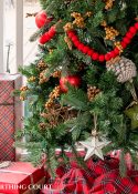 bottom corner of skinny Christmas tree on a screen porch decorated with outdoor type ornaments