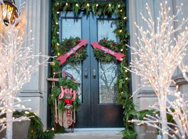 A garland of fresh greenery is around the front door with a sign that says joy.