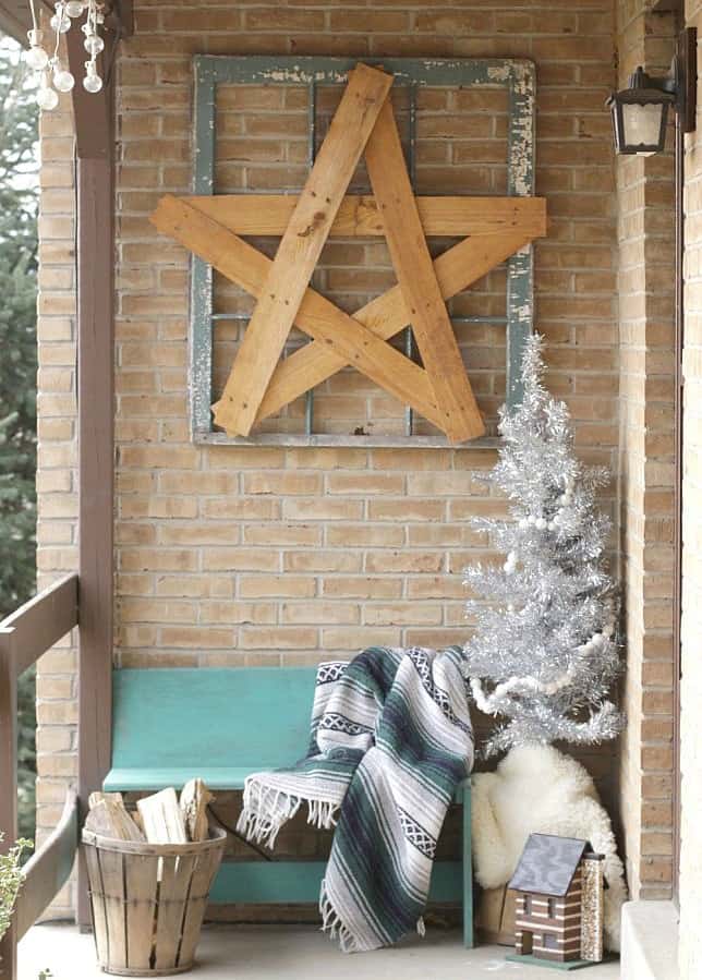 A wooden star in a picture frame is above a sitting bench on the porch.