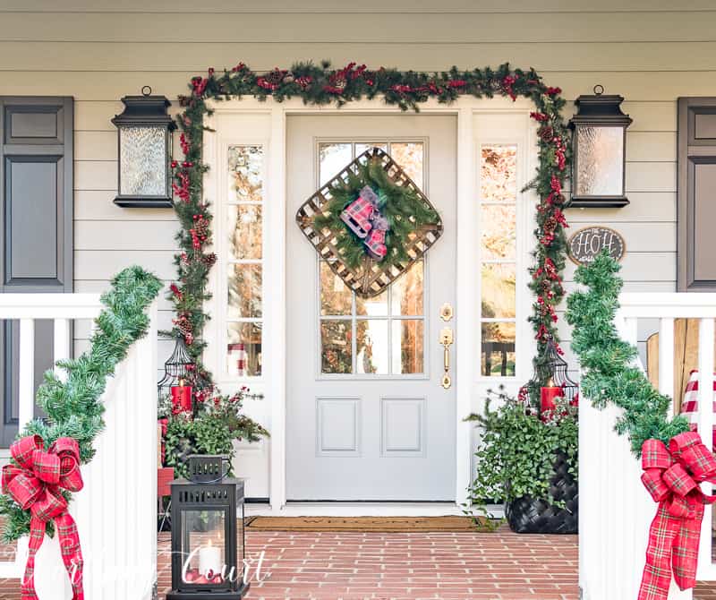 Festive Christmas front porch decorated with red and green with large plaid bows on the front of the stair railing.