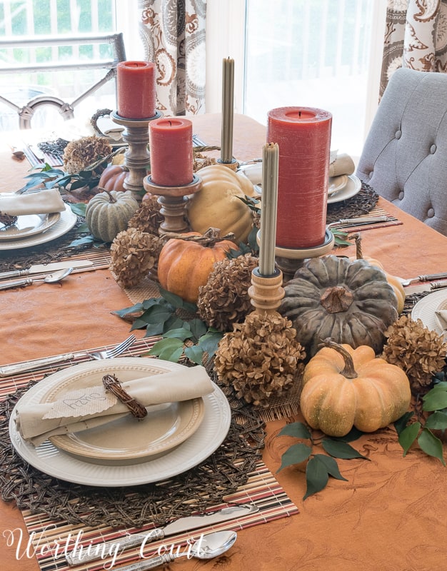 A table set for Thanksgiving with red candles and neutral plates.