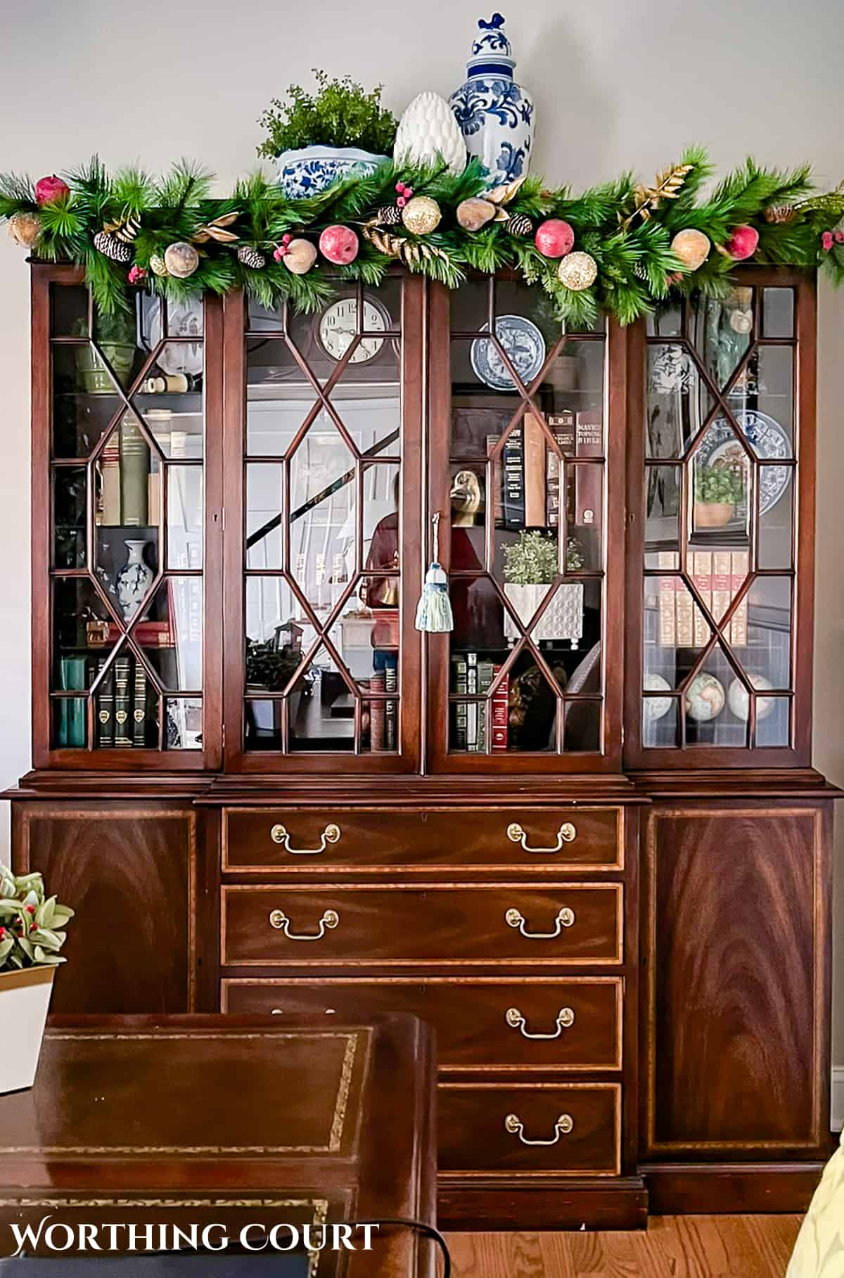 wood china cabinet with glass doors with a Christmas garland across the top