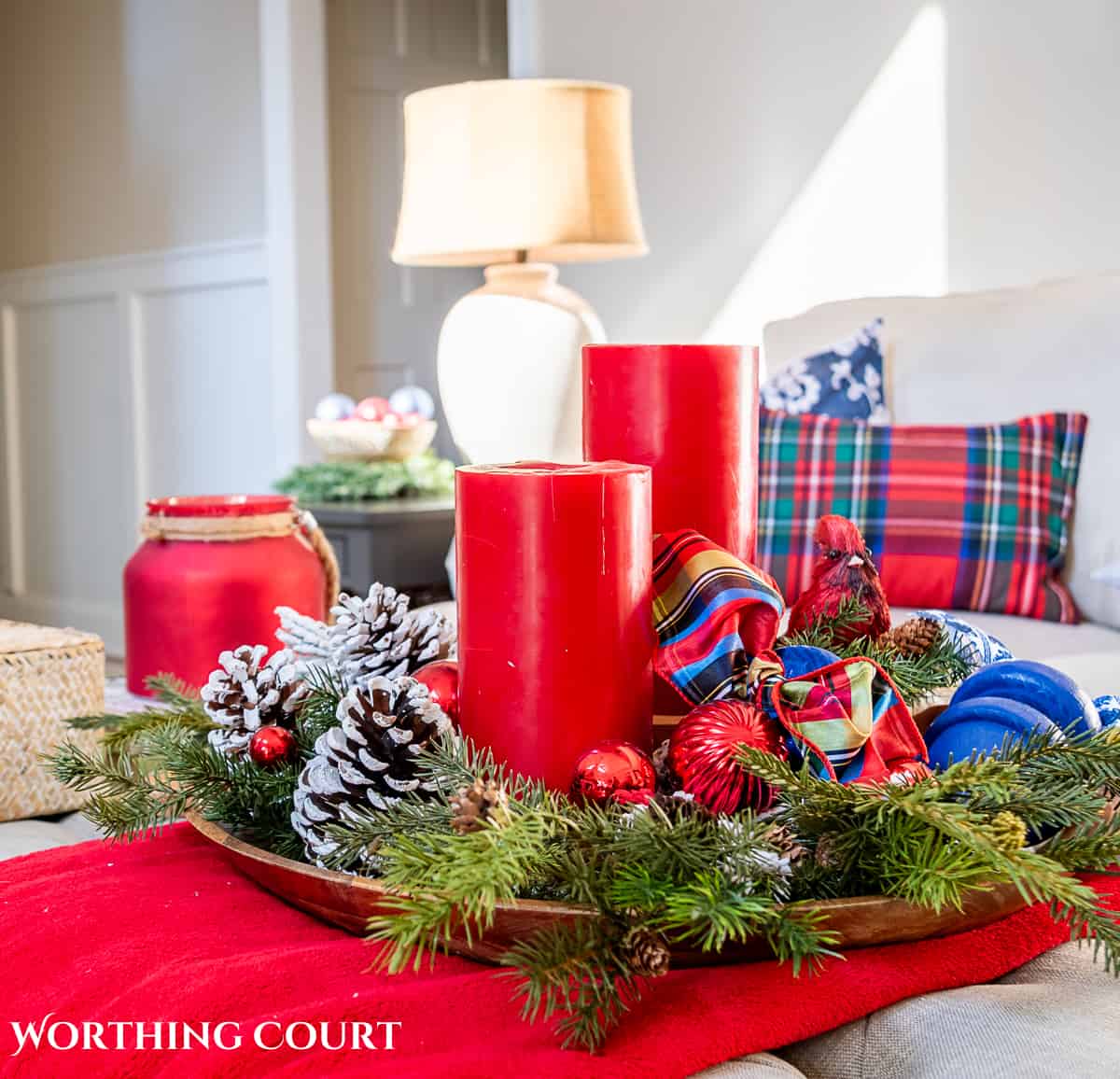 round wood tray on a coffee table filled with red candles, bits of greenery, oranaments and a piece of ribbon.