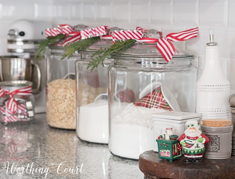 Glass kitchen canisters with faux greenery and Christmas ribbon.