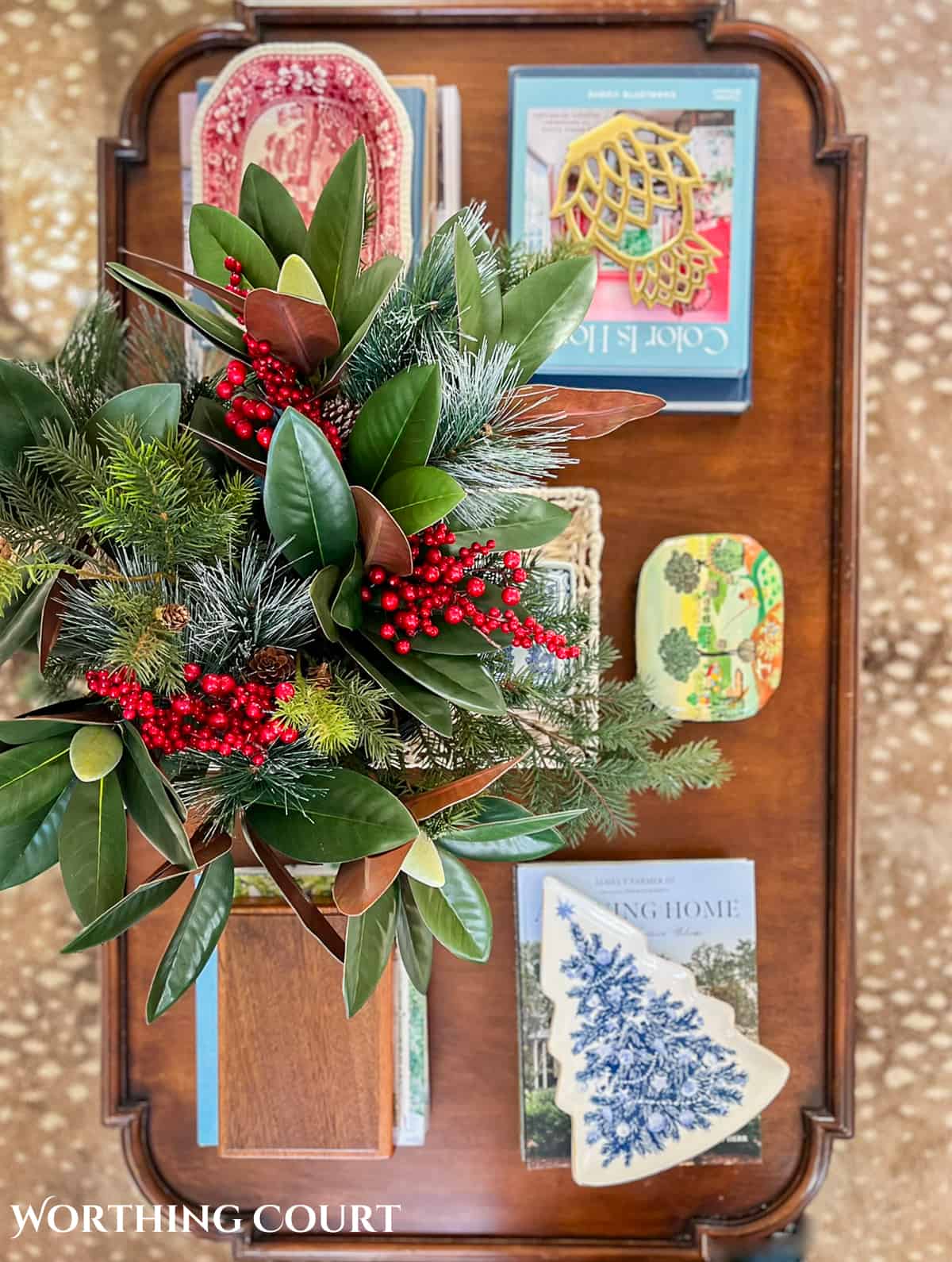 wood coffee table filled with easy decorations for Christmas consisting of coffee table books, Christmas dishes and a bowl filled with faux greenery and berries