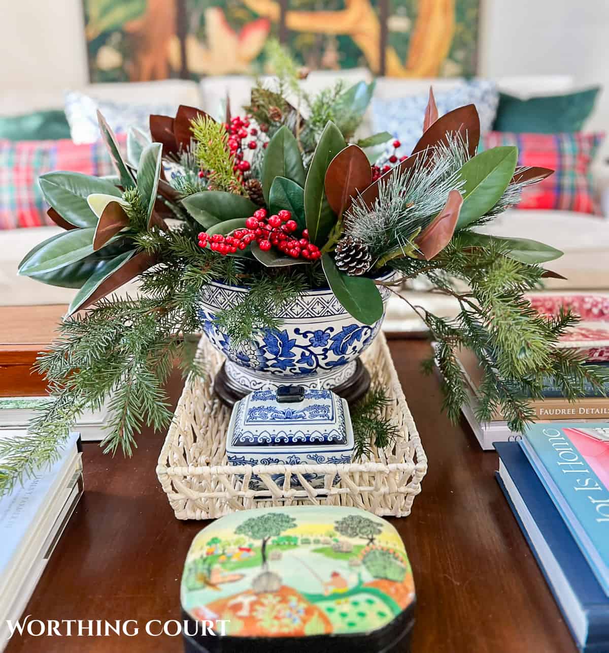 large blue and white container filled with faux greenery and red berries for Christmas on a wood coffee table