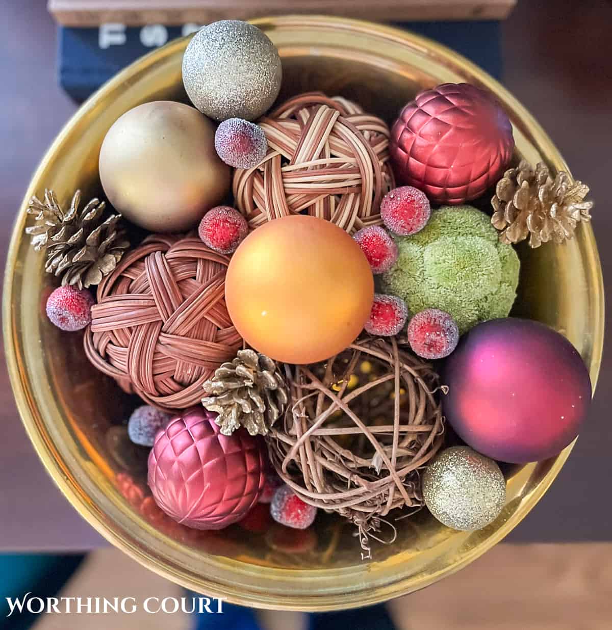 brass bowl filled with wicker and greenery orbs, Christmas ornaments and pine cones.