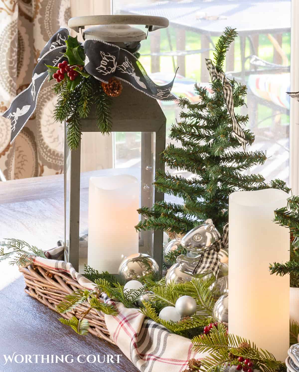 wicker tray on a table with a lantern, candles, mini Christmas trees