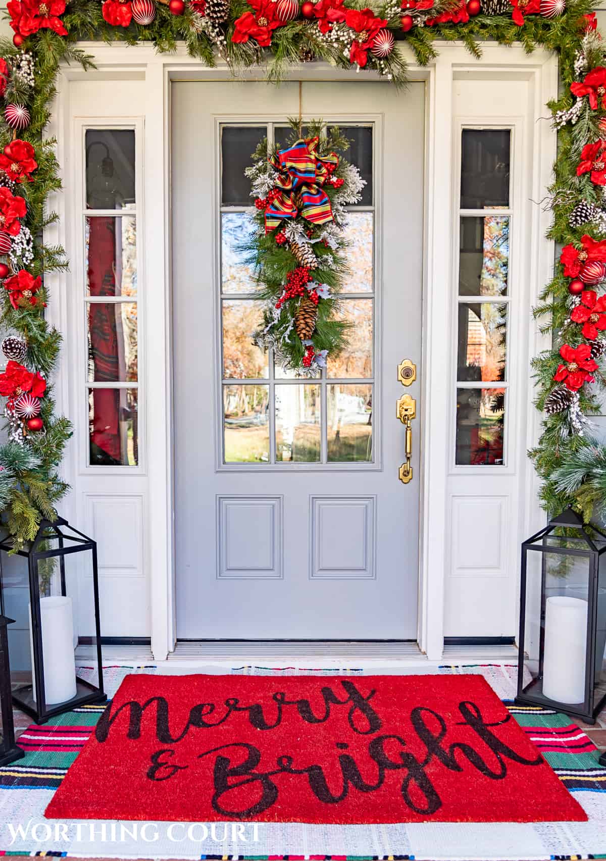 gray front door with glass panes and white sidelights surrounded by a Christmas garland