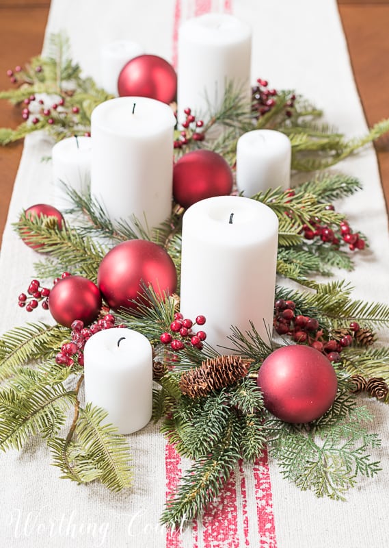 Christmas centerpiece with faux greenery, white candles, red berries and red Christmas tree ornaments #christmasdecor #centerpiece