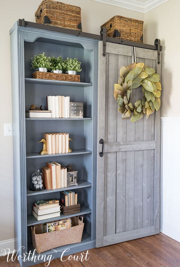 Fake cherry finish bookcase farmhouse makeover in a gray/blue colour with a leaf wreath on it.