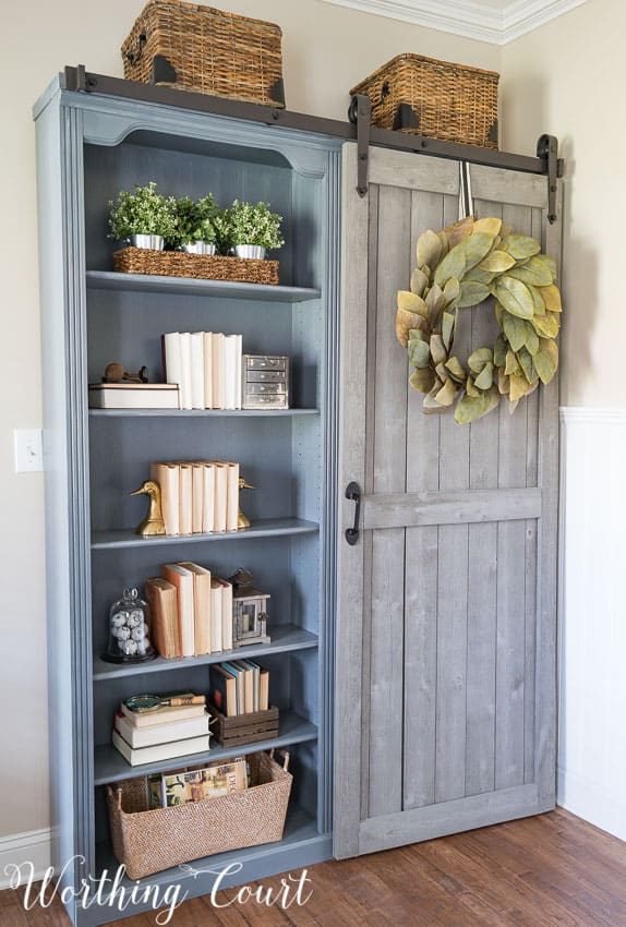 Fake cherry finish bookcase farmhouse makeover in a gray/blue colour with a leaf wreath on it.