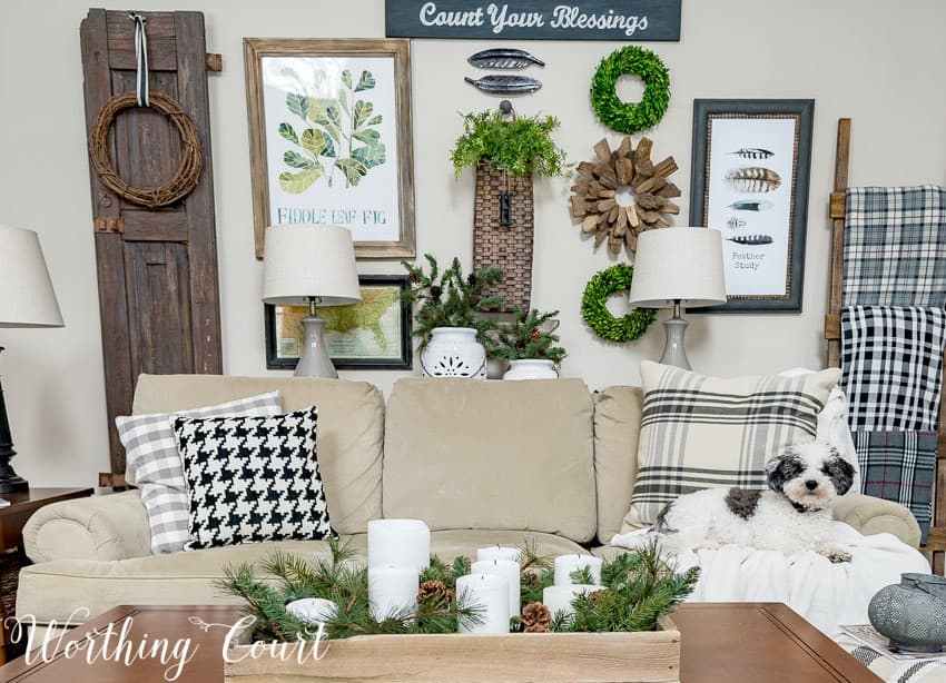 The living room with a neutral couch and throw pillows on the couch, a candle display on the coffee table and wreaths on the wall.