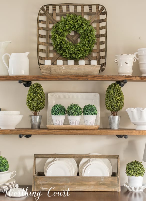 A bright green wreath on a wooden tray on the shelf in the dining room.