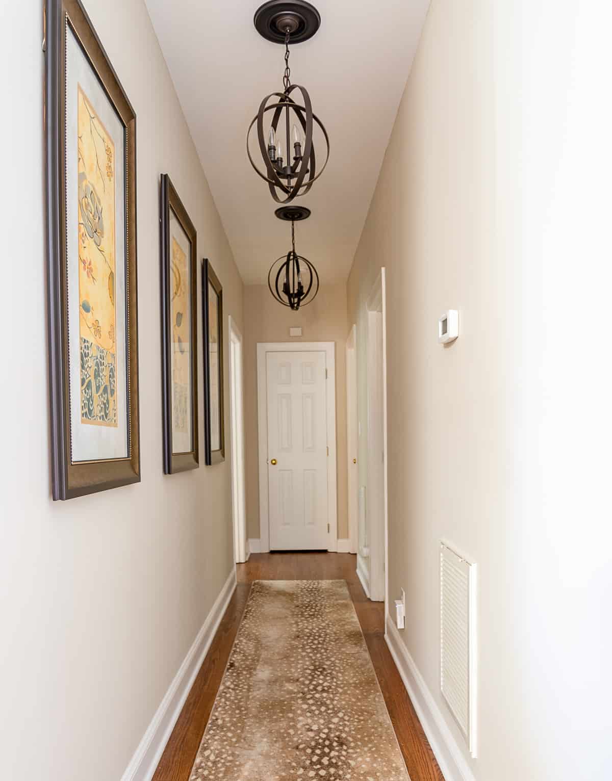 looking down a long hallway decorated with a set of 3 art prints and decorative pendant lights