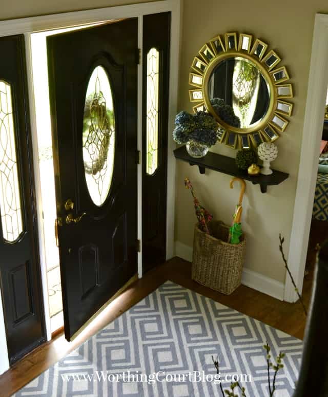 There is a blue and white rug and a sunburst mirror at the entryway.