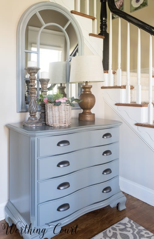 The chest in the foyer with a lamp and a candlestick on top.