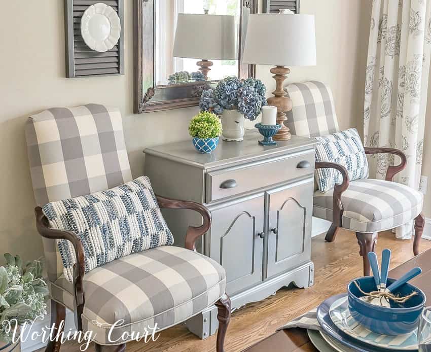 A small table in between two chairs in the sitting room with faux and fresh flowers on it.