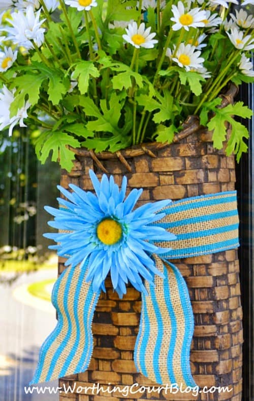 A bright blue ribbon with a faux flower is tied around a basket of daisies.