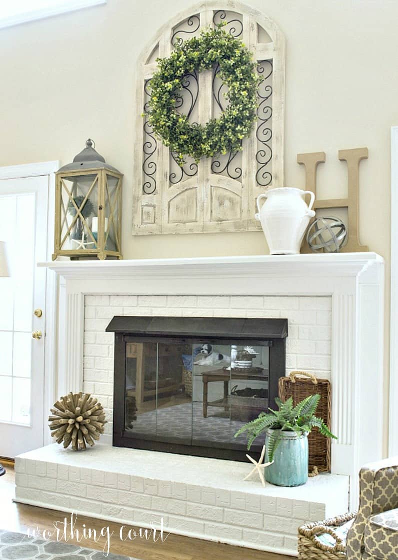 Red brick fireplace with oak surround and mantel painted white and brass fireplace screen painted with high temp spray paint. Tall ceilings with arch window wall decor above mantel. #farmhousedecor #makeover #diy #paintedfireplace #manteldecor #fireplacedecor #paintedbrick