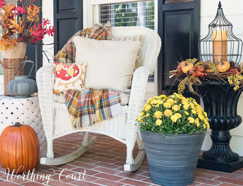 Outdoor chair with a fall throw and fall throw pillows beside a planter full of yellow moms.