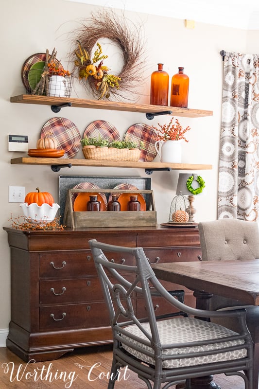 Kitchen shelves decorated with plaid plates, amber glass and a fall wreath.