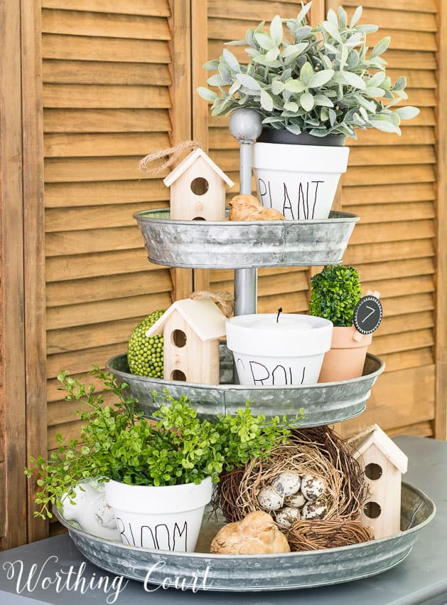 tiered tray decorated for spring with birdhouses flower pots and greenery