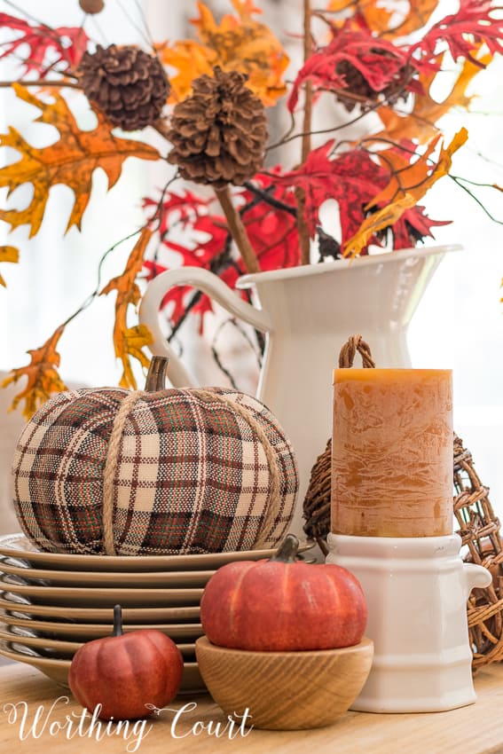 Fall centerpiece with a plaid pumpkin, small faux pumpkins and fall colored candle.