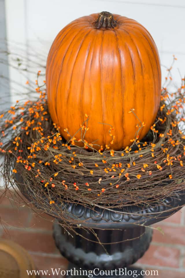 outdoor urn decorated for fall with large faux pumpkin and grapevine wreath