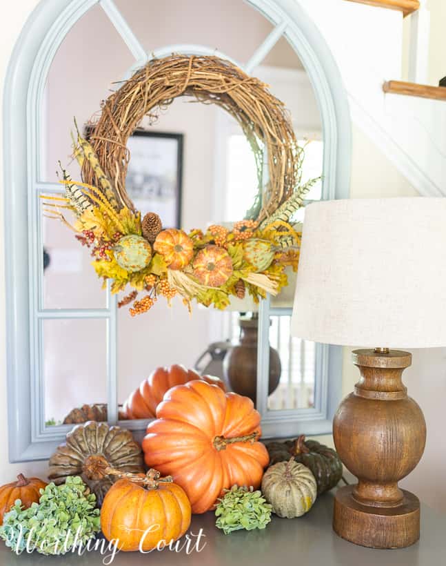 Variety of pumpkin colors displayed together on a small chest, with a fall wreath hanging on a mirror above the chest.