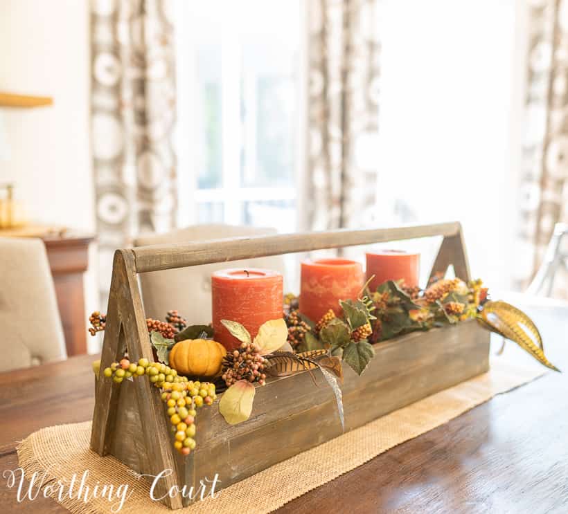 There is a vintage wooden toolbox filled with candles, mini pumpkins, and leaves on the table as a centerpiece.