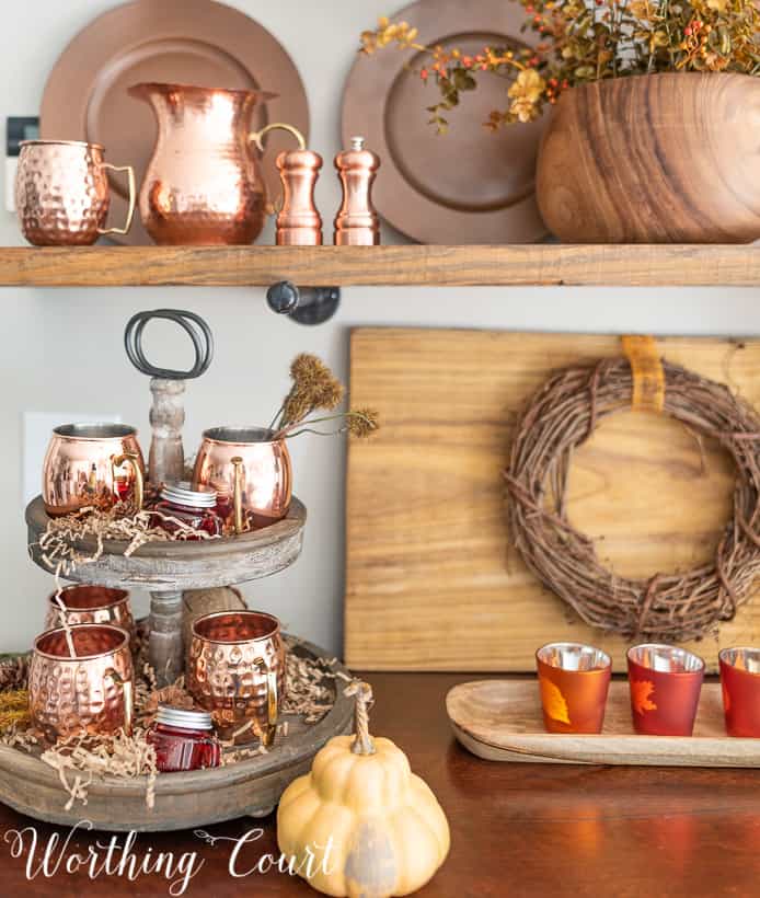 The Moscow mule cups are on a wooden tiered tray that is on the hutch.