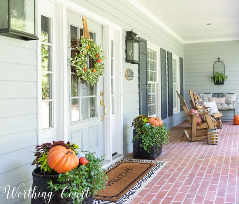 There is a fall wreath on the front door and pumpkins in planters beside it.
