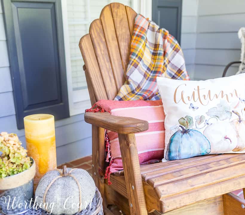 Front porch with fall decorations such as a pillow that says autumn, and pumpkins and candles.