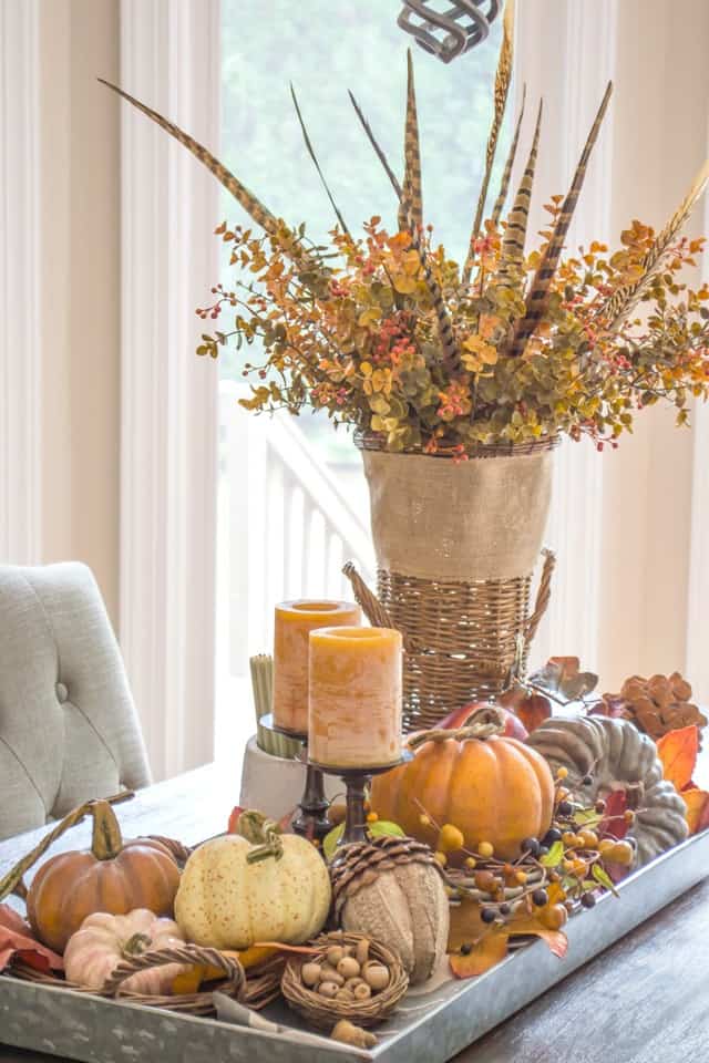 Fall centerpiece in a metal tray with fall foliage, candles, pumpkins and feathers.