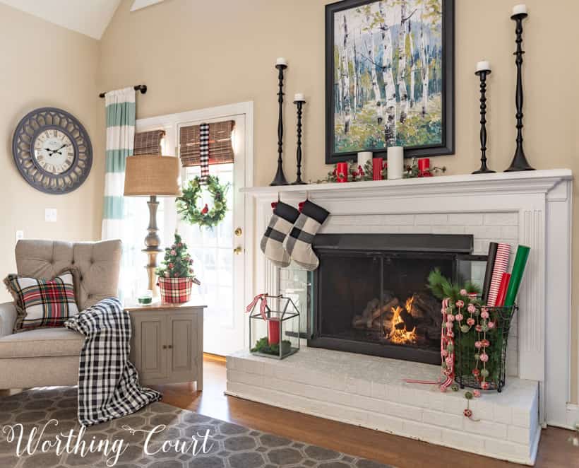 A lit fireplace in the living room with wire basket on one side and a candle on the other side.