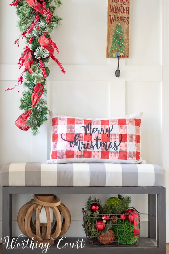 A wire basket is underneath the bench filled with Christmas decor.