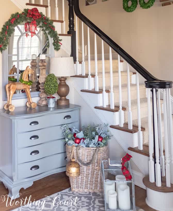 A dresser beside the stairs with a mirror on it and a basket beside it.