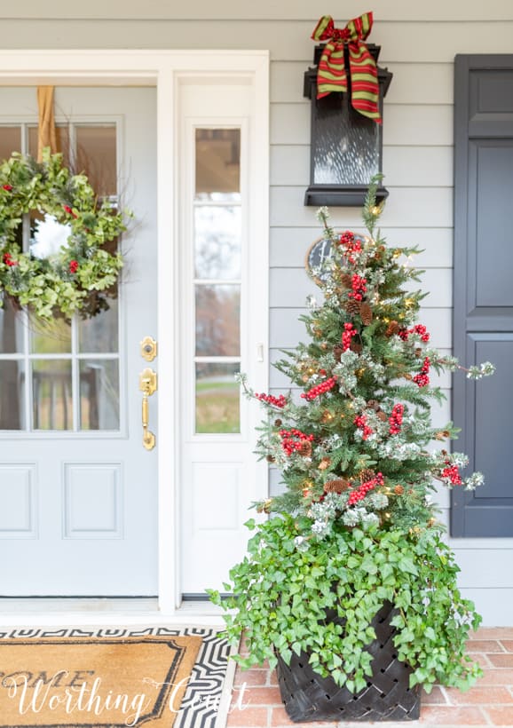 The Christmas tree has red berries on it.   There is a bow on the outdoor light.