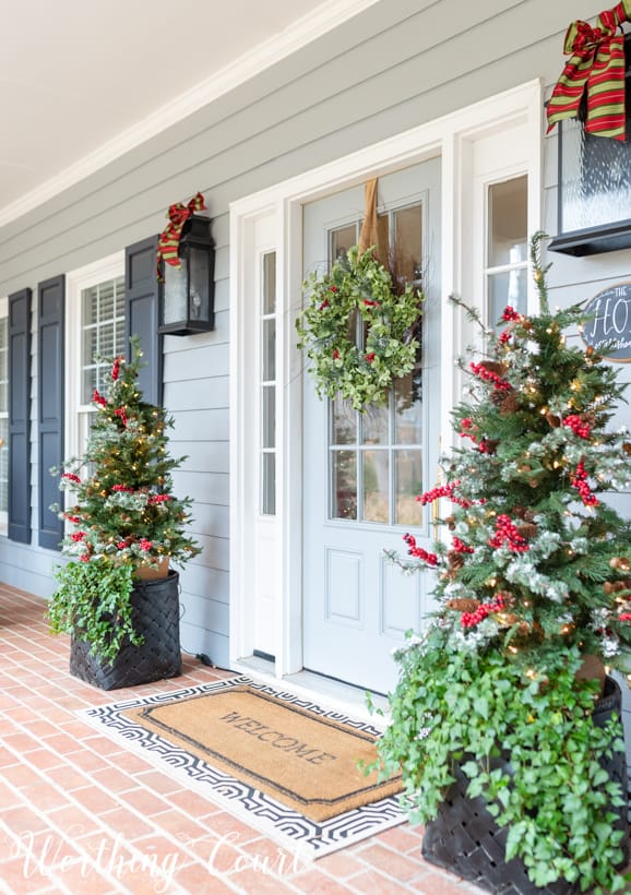 Christmas front porch decor with little Christmas trees flanking the front door.