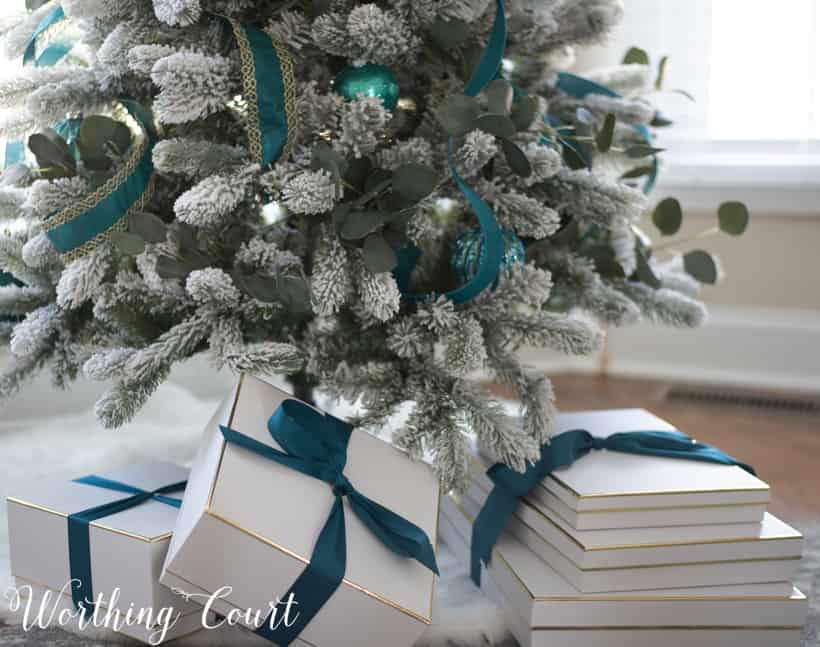 White gift boxes on a fur Christmas tree skirt with teal ribbons on the presents.