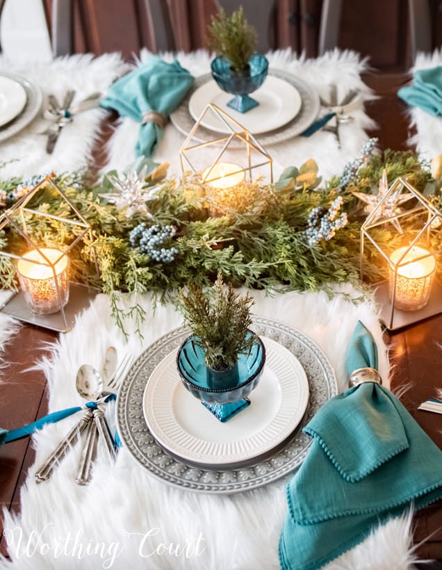 There are white plates, blue glass dishes and a sprig of greenery in the blue glass.