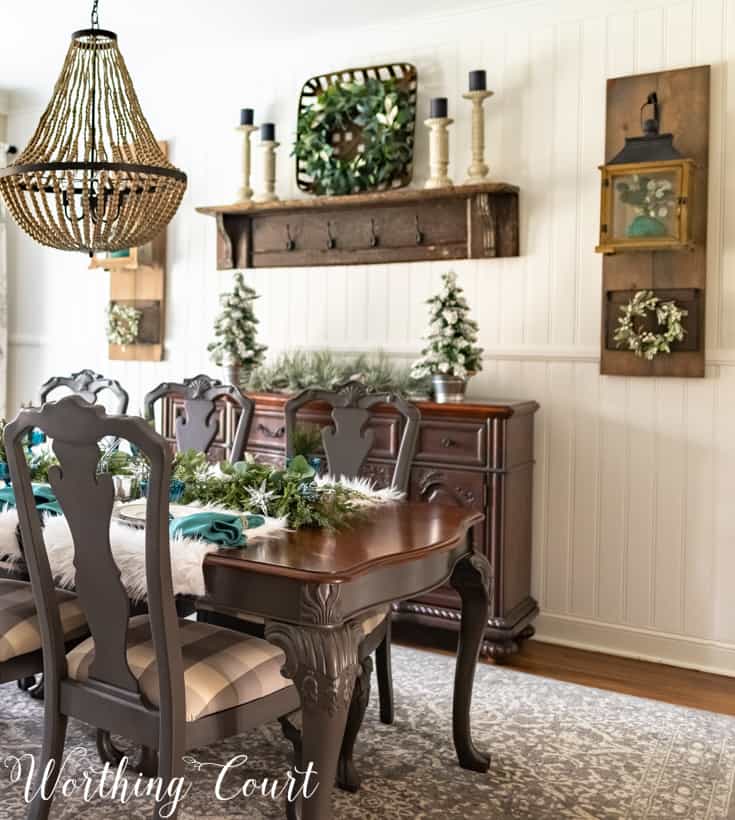 There is a wooden hutch on the wall with a small wooden rustic shelf above it and candlesticks on the shelf.